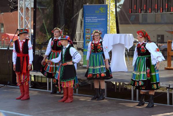 Fünf Mitglieder einer Folkloregruppe in bunten Trachten stehen bei einem deutsch-polnischen Erntedankfest auf der Bühne.