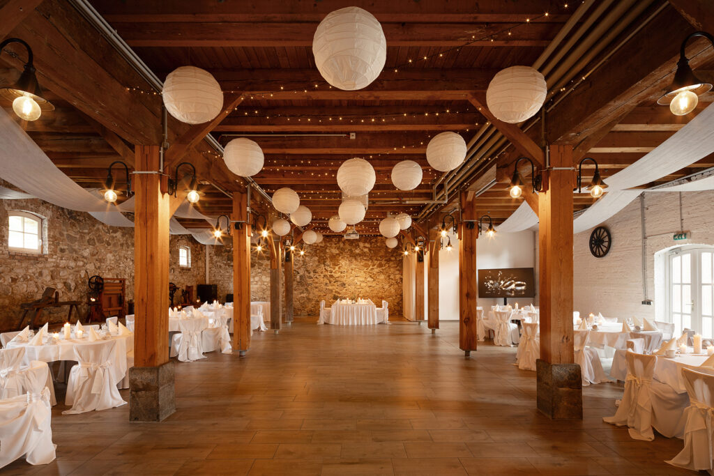 Rustikaler Festsaal im Hotel Landhof Liepe mit gedeckten Tischen, Holzdecke, Kronleuchtern und festlicher Dekoration