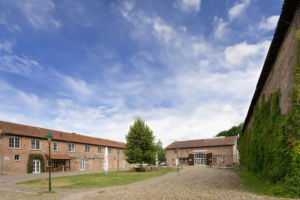 Historischer Innenhof des Landhofs Liepe mit roten Backsteingebäuden, begrünten Mauern, Kiesweg und altem Baumbestand