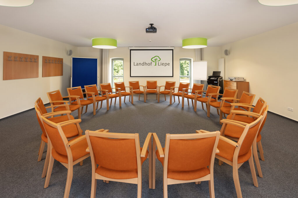 Heller Seminarraum im Hotel Landhof Liepe mit orangefarbenen Stühlen im Kreis und Leinwand mit Logo