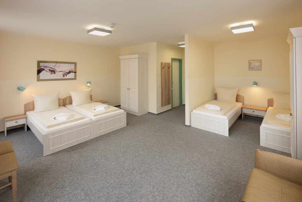 Helles Standardzimmer im Hotel Landhof Liepe mit zwei Einzelbetten, zwei weiteren Betten, Schränken und Sitzplätzen