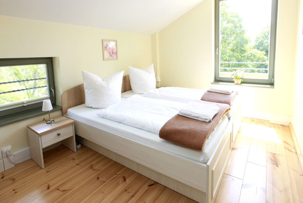 Helles Doppelzimmer im Hotel Landhof Liepe mit weißem Bett, Holzboden, Sitzfenster und Blick ins Grüne