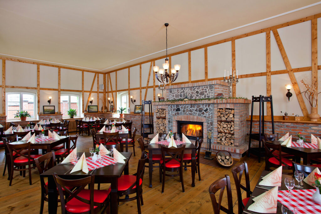 Rustikales Restaurant von Landhof Liepe mit gedeckten Tischen, roten Stühlen und offenem Kamin in regionaler Atmosphäre.