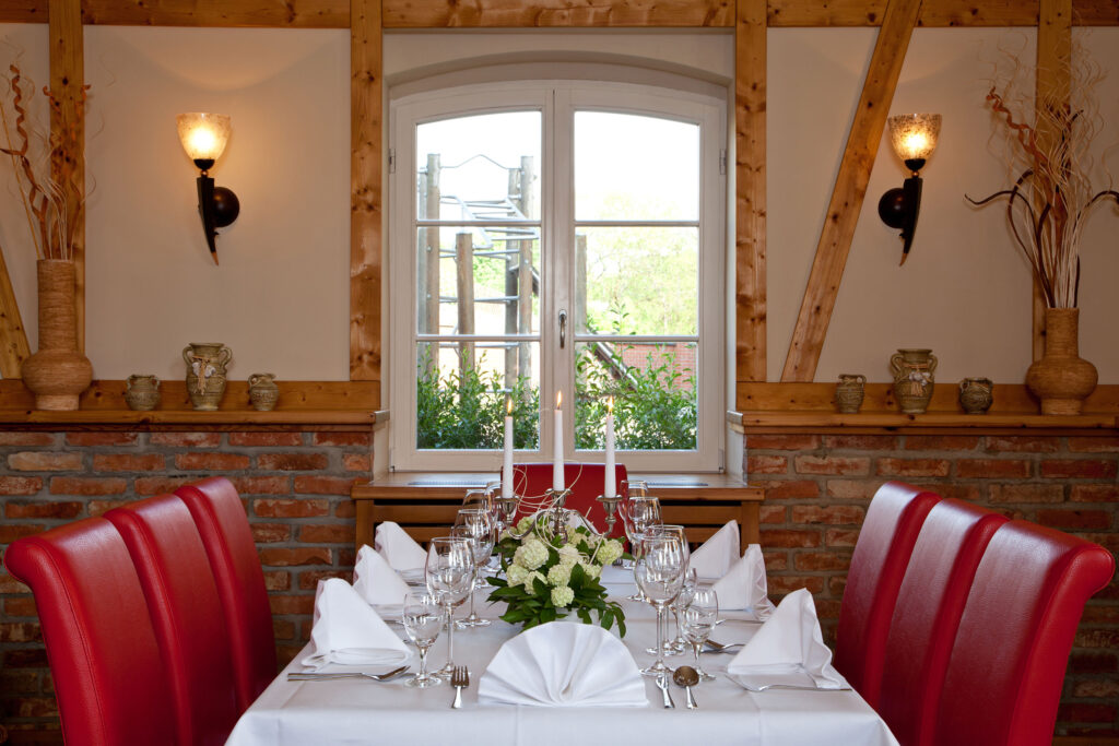 Festlich gedeckter Restauranttisch mit Blumen, gefalteten Servietten und roten Polsterstühlen im rustikalen Ambiente