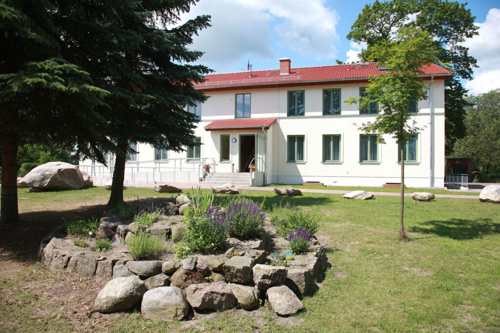Das Gebäude von Landhof Liepe mit rotem Ziegeldach, grünen Fenstern und gepflegtem Garten für Familienangebote