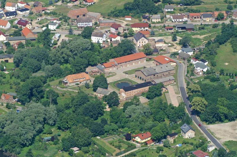 Luftaufnahme von Landhof Liepe mit historischen Gebäuden, begrünten Außenflächen und der Straße durch das Dorf Liepe